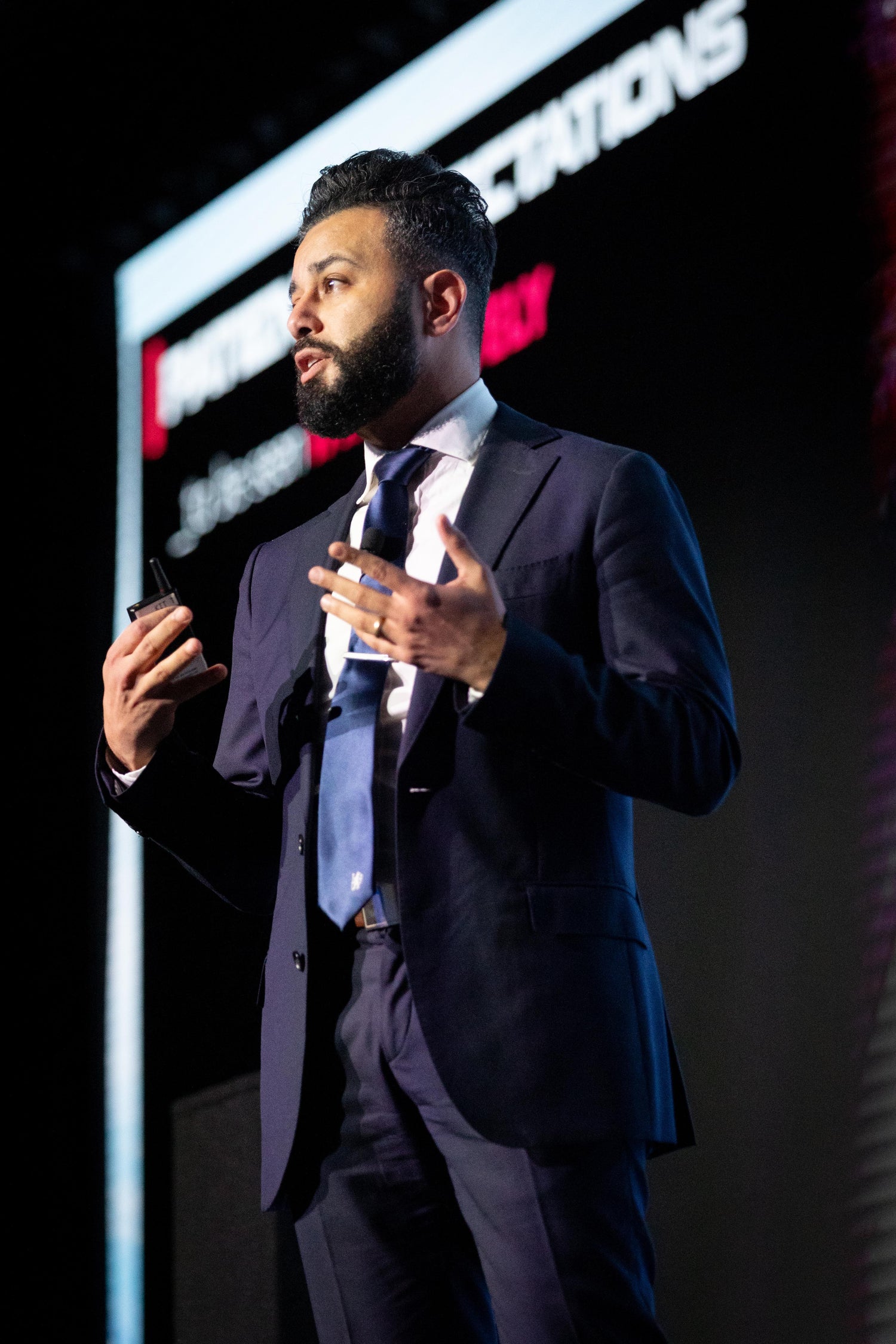 Dr. Attia in a suit giving a presentation on a stage with a dark background